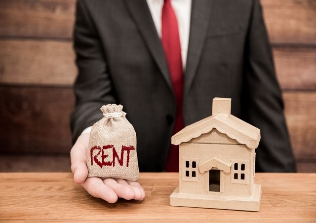 business-person-holding-a-bag-of-money-with-the-word-rent-on-it-and-wooden-toy-house