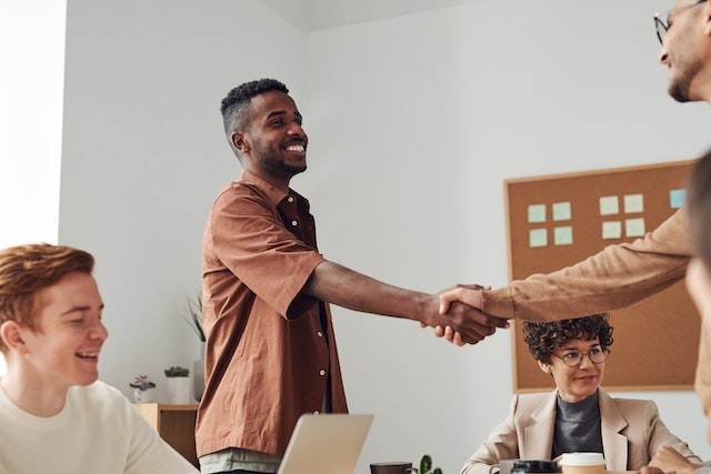 two people standing over a table shaking hands with two others sitting